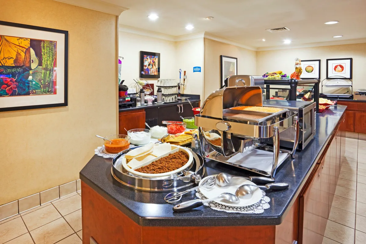 A lively hotel dining area showcasing a colorful breakfast buffet spread and a dedicated coffee station. Guests can be seen enjoying breakfast and socializing amid vibrant artwork, creating a welcoming and communal dining environment.