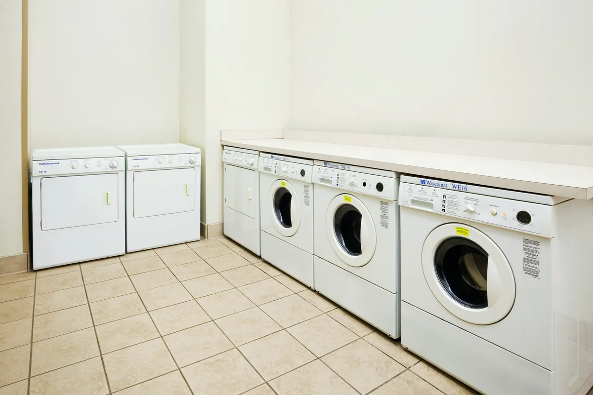 The photo features a tidy laundry area with modern washing machines, dryers, and a functional countertop for sorting and folding clothes. The environment is clean and organized, suggesting ease and convenience for guests.