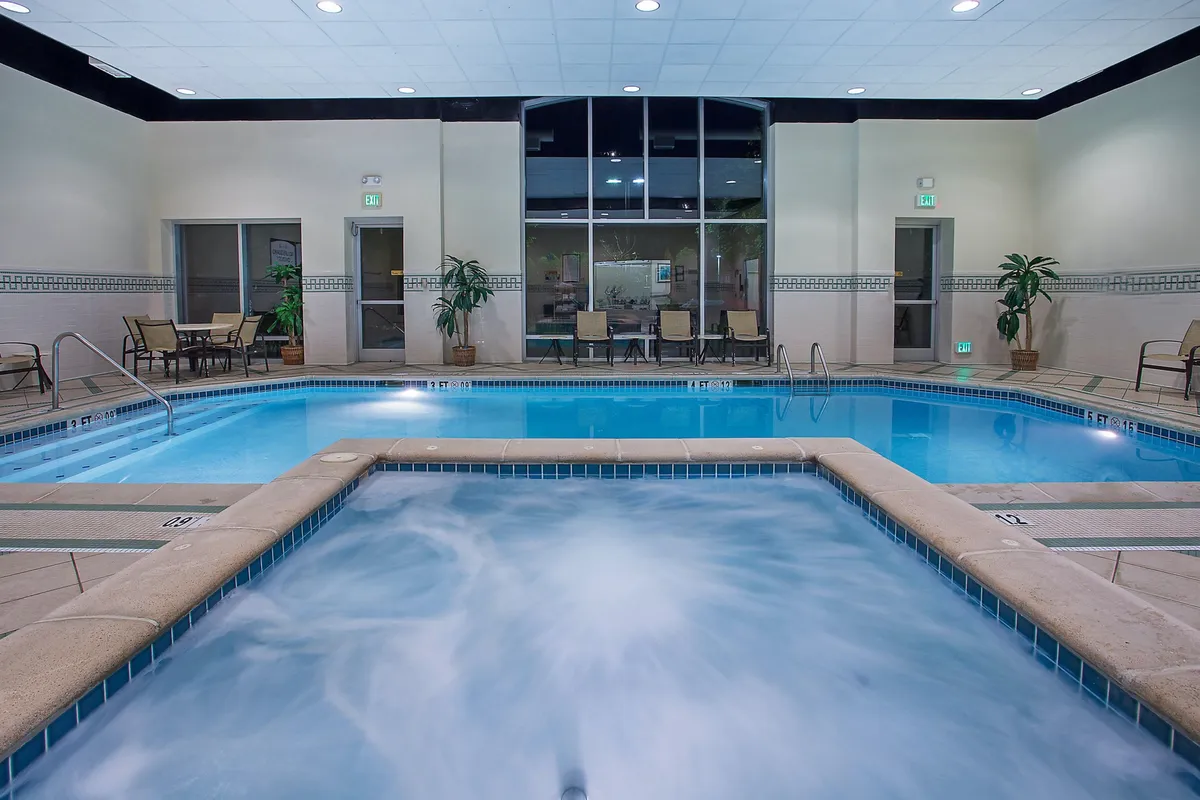 This image captures a tranquil indoor pool and hot tub area, accented by lush indoor plants and comfortable lounge chairs. Guests can be seen swimming, relaxing in the hot tub, and socializing in a serene, softly lit environment.