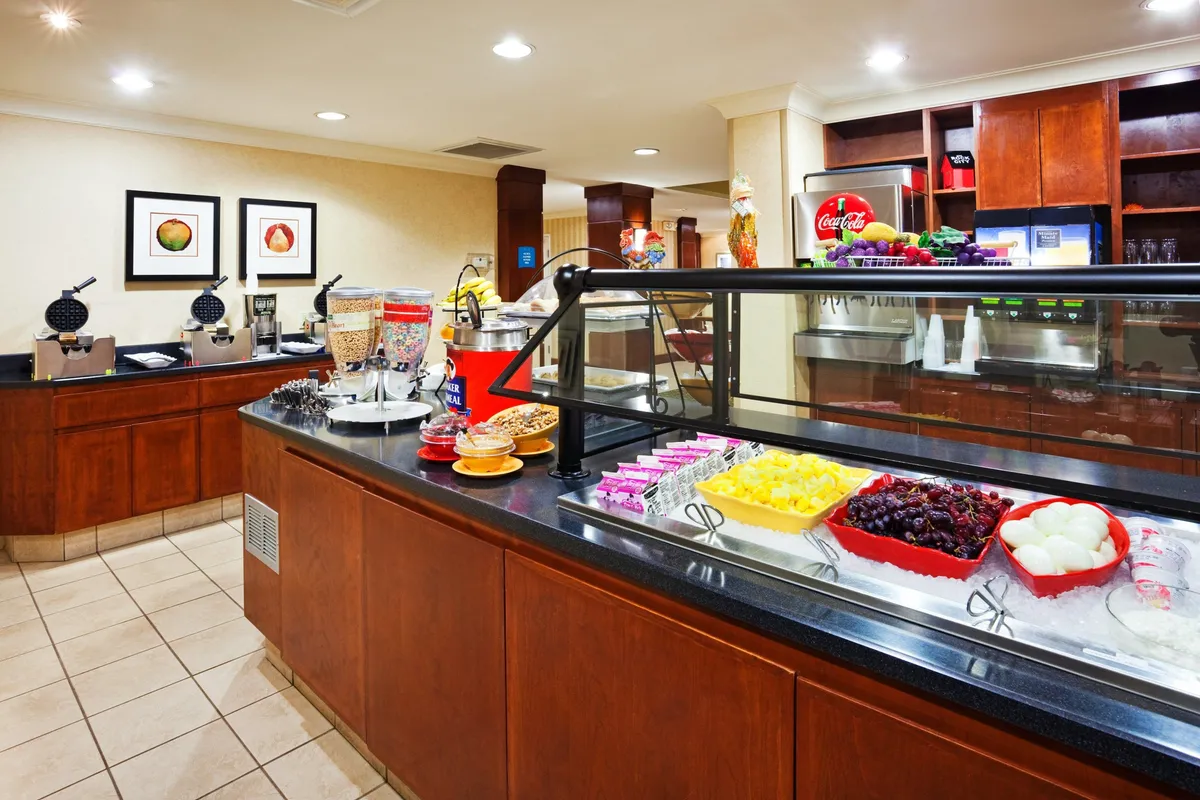 A cheerful breakfast bar with an array of food displays, a coffee station, and colorful artwork. The setting is friendly and relaxed, encouraging morning routines or social interactions.