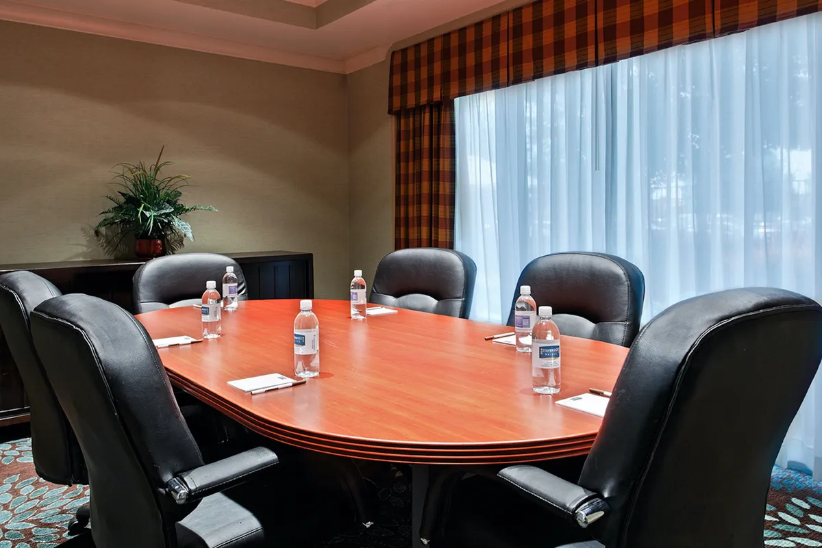 A well-appointed conference room with an oval table surrounded by black leather chairs, notepads, bottles of water, and a bright, collaborative atmosphere, ideal for business meetings and brainstorming sessions.