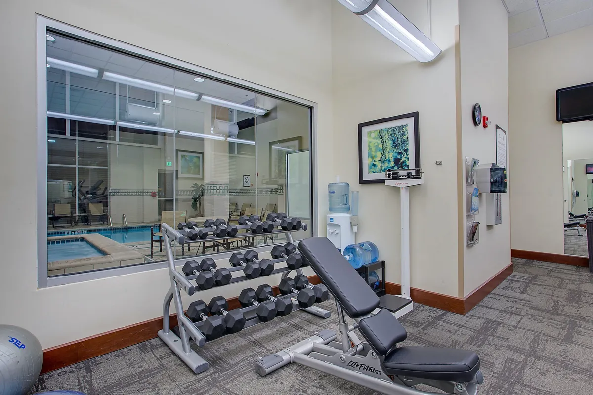 A vibrant fitness center featuring a dumbbell rack, weight bench, water cooler, and motivational artwork on the wall. The space is inviting for both solo workouts and group classes, emphasizing wellness and balance during business travel.